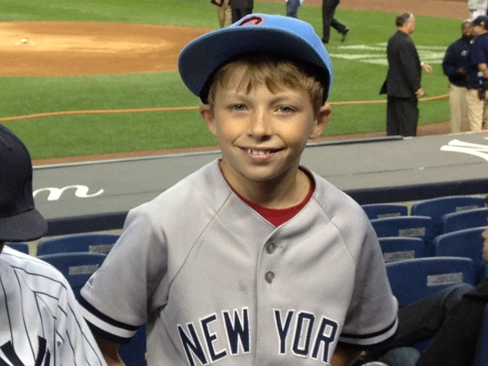 Young Jack at the ballpark wearing a New York baseball jersey and blue cap